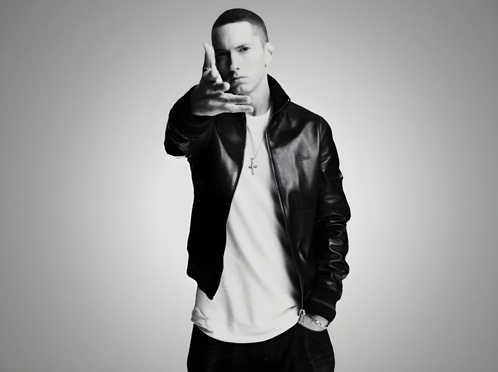 Eminem posing in a black leather bomber jacket looks into the camera