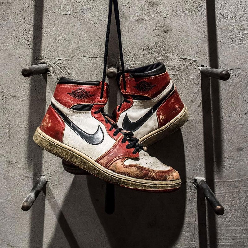 Paio di sneakers da basket appese dai lacci, Air Jordan 1 OG Chicago colorway White/Red/Black rovinate dal tempo e dall'usura sul campo da gioco