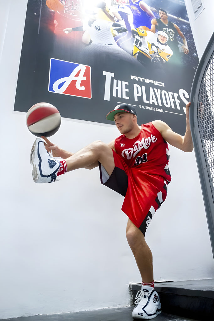 Ragazzo atleta della DaMove Crew vestito con divisa ufficiale rossa della loro squadra intento ad eseguire una mossa acrobatica di street basketball mentre fa roteare una palla da basket sulla punta del piede