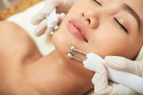 Photo femme en séance d'électrostimulation dans un institut de beauté avec deux appareils de microcourants sur les joues