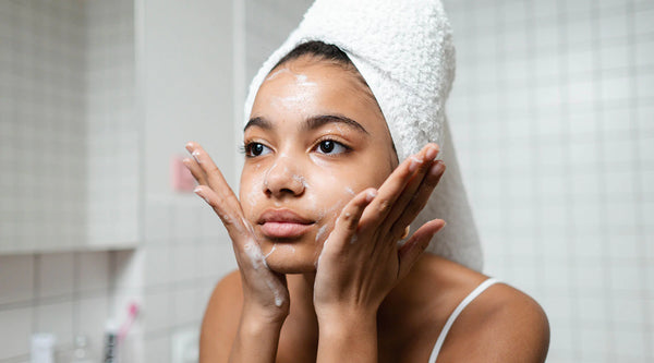 Visage d'une Femme métisse dans une salle de bain blanche qui se nettoie le visage avec de la crème
