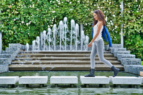 Eine Frau in Barfußschuhen läuft auf einem Weg, der durch einen Springbrunnen führt.