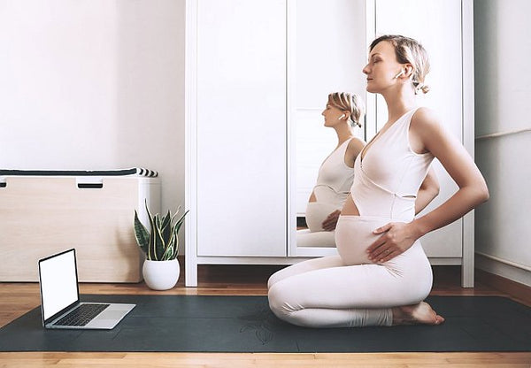 Pregnant woman kneeling on a yoga mat listening to headphones