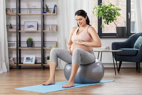 Pregnant woman sat on exercise ball holding her baby bump