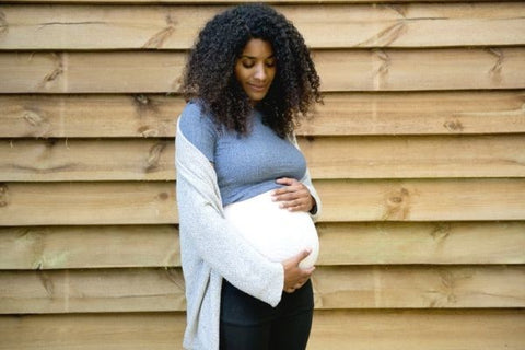 Pregnant woman holding bump whilst wearing Secret Saviours Stretch Mark Prevention Band