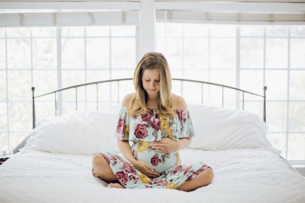 Pregnant woman sat on bed thinking about body image post pregnancy