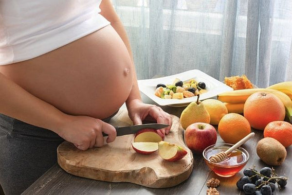 pregnant woman chopping fruit with baby bump exposed
