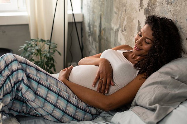 2 Pregnant woman lying on a bed hugging her baby bump