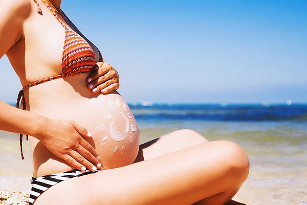 Pregnant woman sat on beach applying sun cream