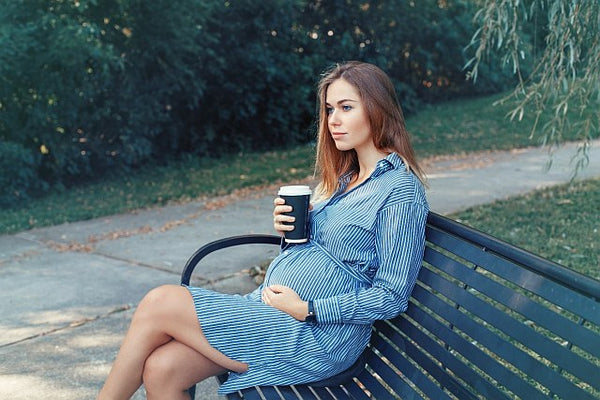 3. pregnant lady sat on a park bench drinking coffee