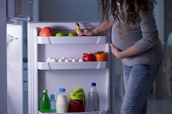 4. pregnant lady standing at an open fridge looking at food inside