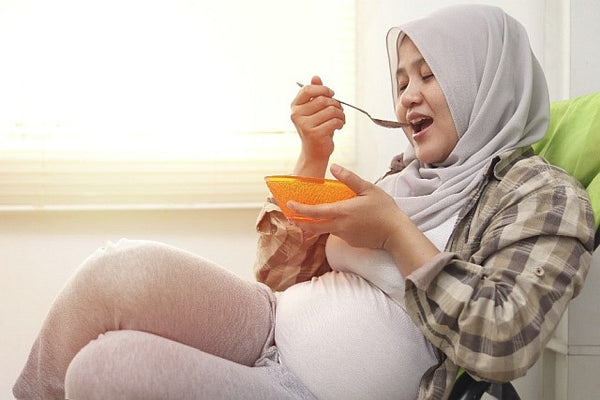 pregnant woman eating from an orange bowl