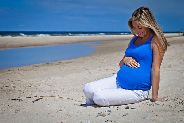 pregnant woman knelt on a sandy beach looking at baby bump