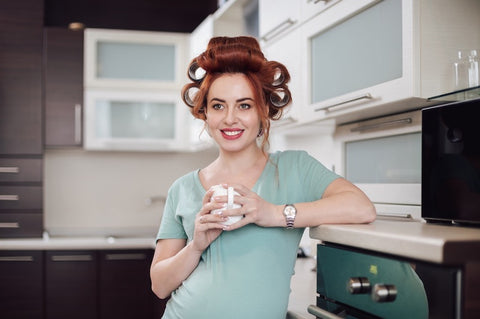 woman with rollers,holding a cup in a kitchen