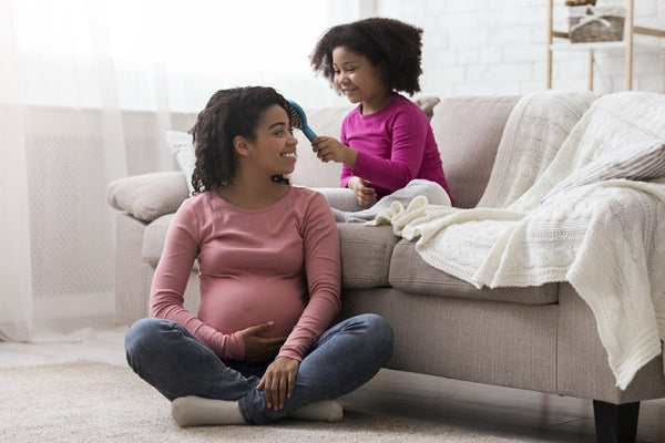 Pregnant mum having her hair brushed by her young daugther