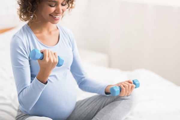 Pregnant woman using small weights sat on bed