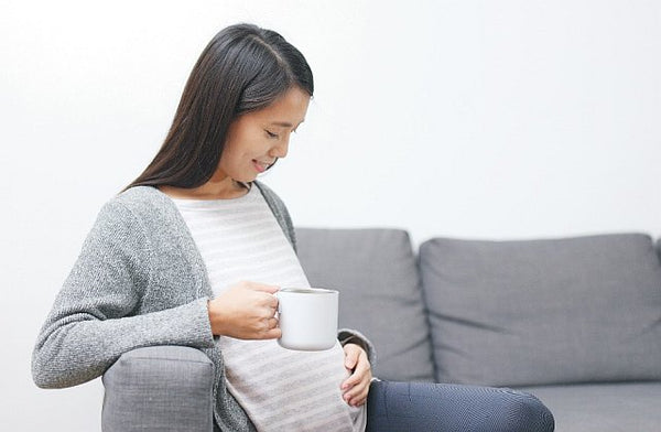pregnant woman looking at her baby bump whilst drinking from a mug