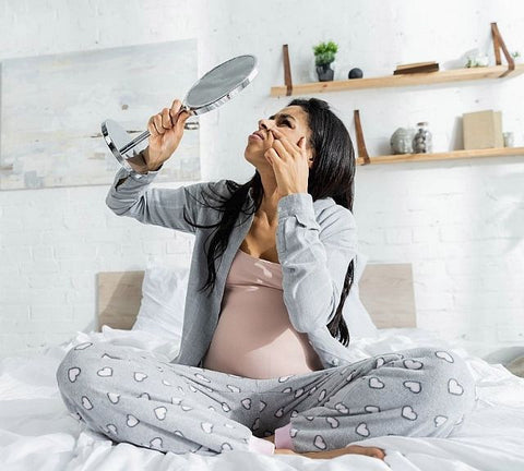pregnant woman looking in hand held mirror at her face
