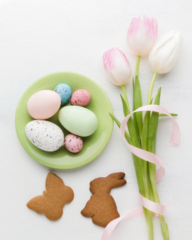 jajka na talerzu obok są tulipany kolorowe ze wstążką i ciastka w kształcie króliczka i motylka