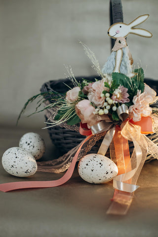 Velikonoční vajíčka ležící vedle velikonočního koše, který je zdoben stuhami