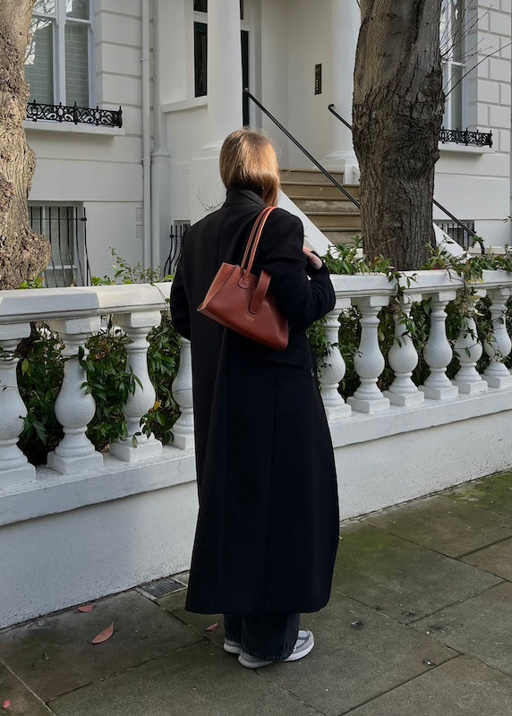 woman wearig a black coat and holding a tan leather bag