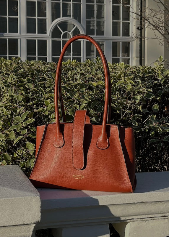 Tan leather bag places on a white stone wall