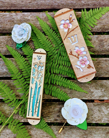 Aspen Tree Mezuzah with light blue background, almond blossom mezuzah, and 2 guitar pick boutonieres on a fern leaf.