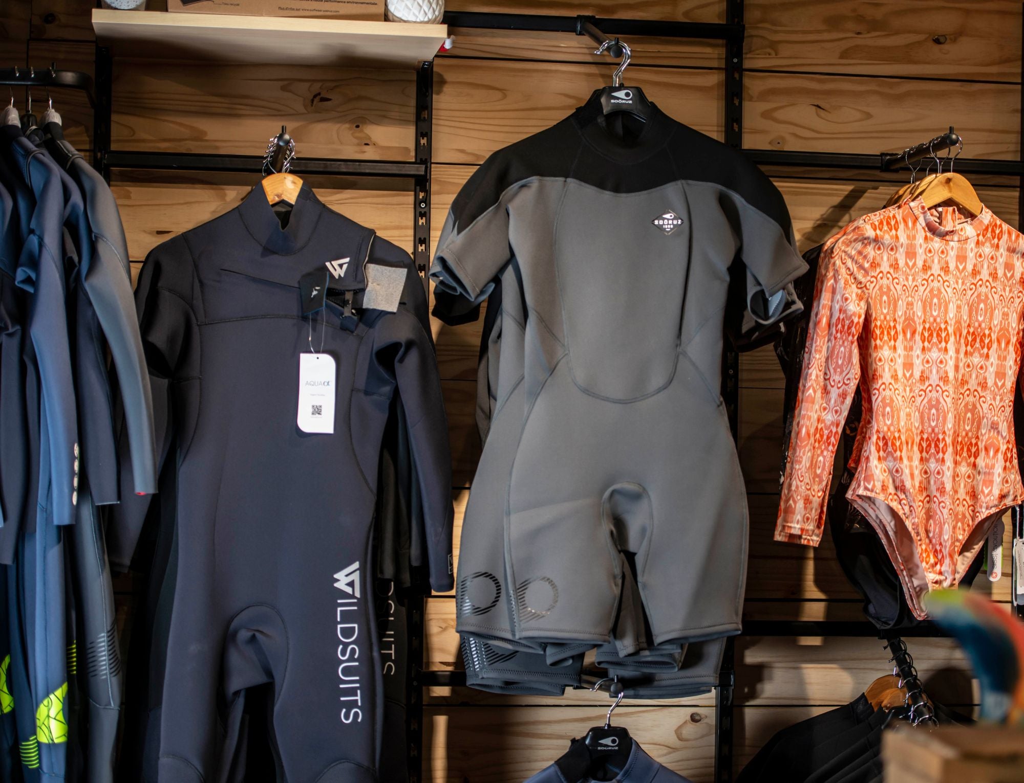 A rack of women's surf wetsuits and men's summer shorties in a surfshop