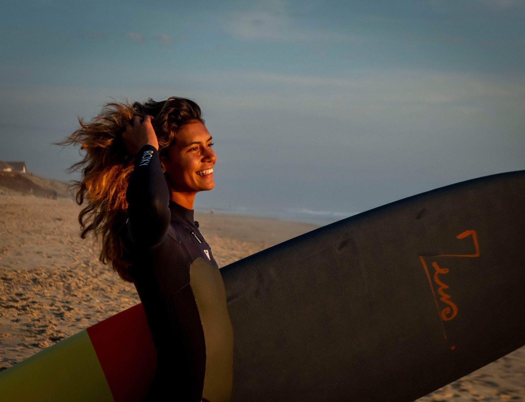 Une femme avec une combinaison de surf intégrale Roxy et une planche de surf Zeus