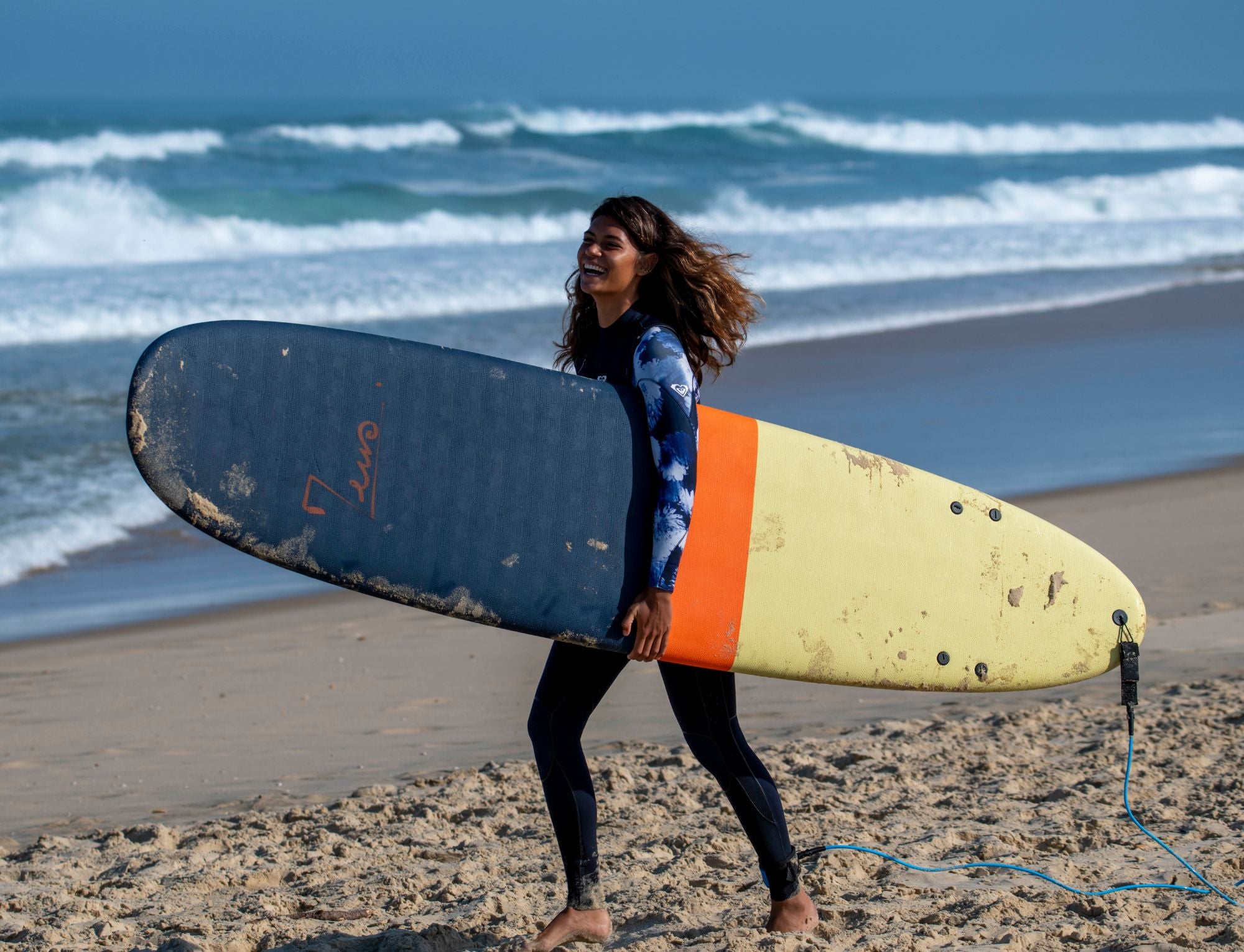 Une surfeuse avec une planche zeus et une combinaison de surf Roxy