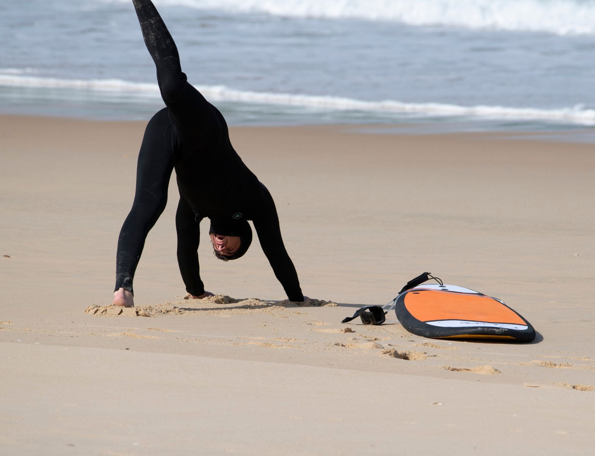 Un surfista con traje de neopreno completo calentando en la playa.