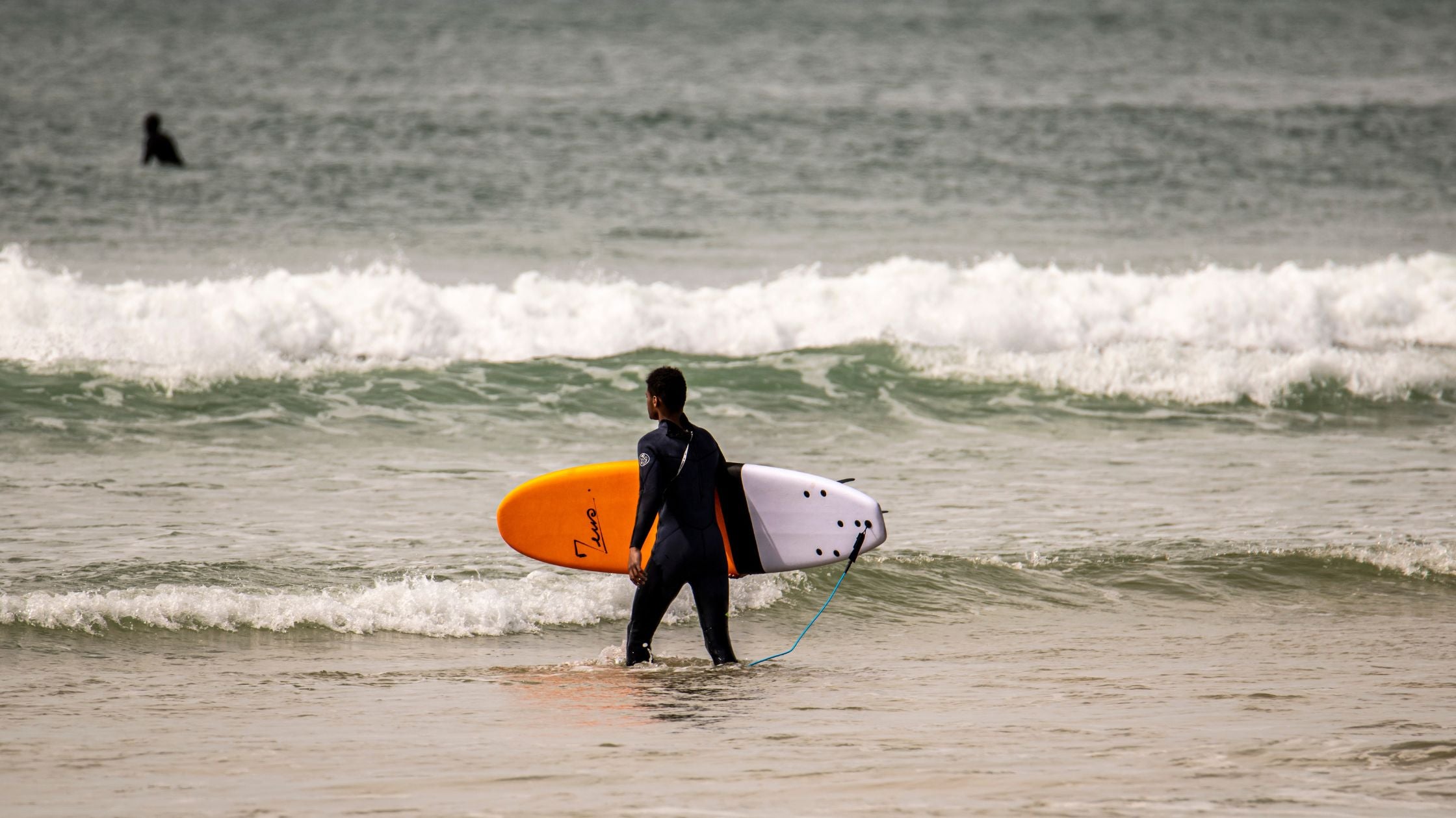 Un surfer débutant en train de se mettre à l’eau avec une planche en mousse orange
