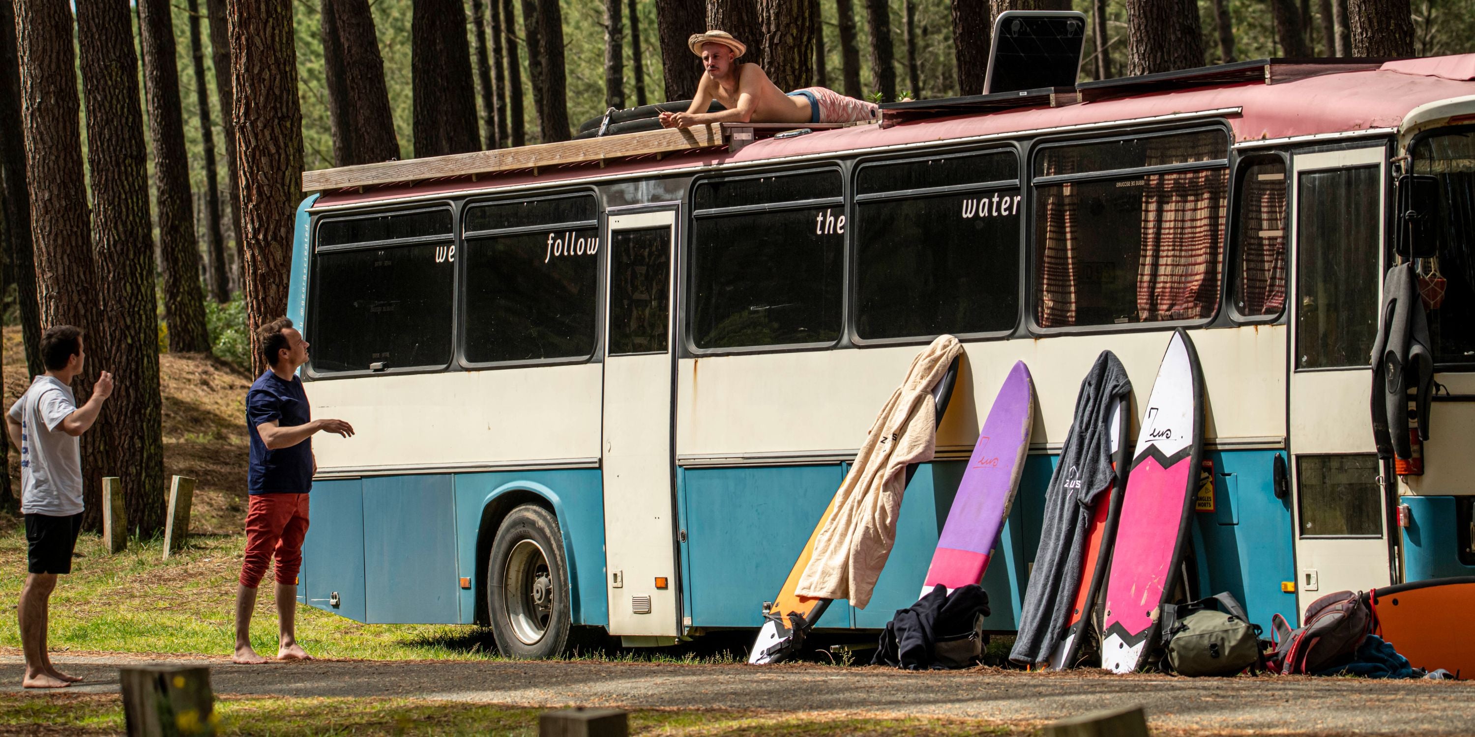 un van dans la foret avec des planches de surf et des ponchos de surf en train de sécher