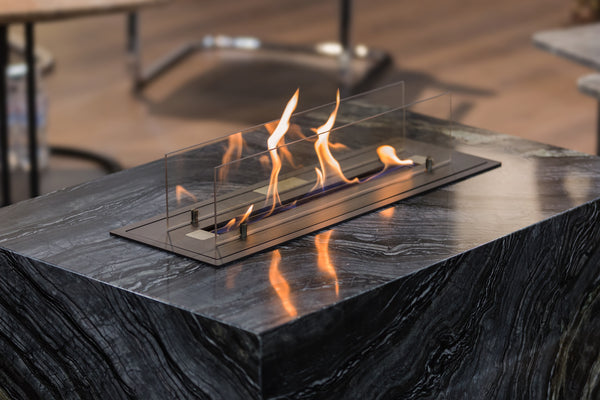 An ethanol burner in a black marble table producing golden-orange flames.