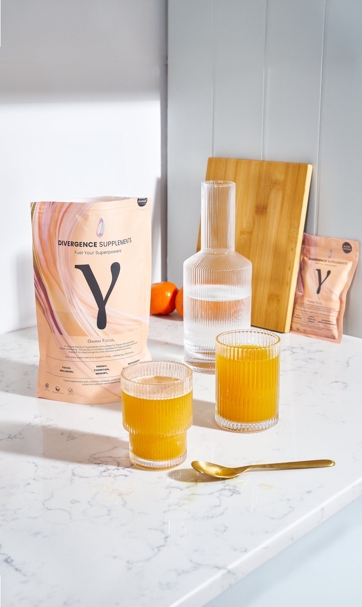 Supplement packages on a kitchen counter with glasses of orange liquid and a gold spoon.