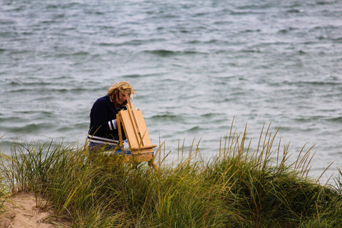 an artist on a beach paints from observation on an easel