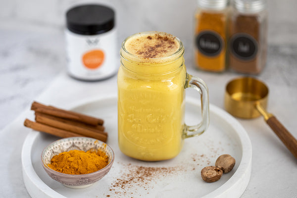 A serving platter with a jam jar containing yellow Golden Milk with cinnamon sticks, a bowl of tumeric powder and the XbyX product Take It Easy