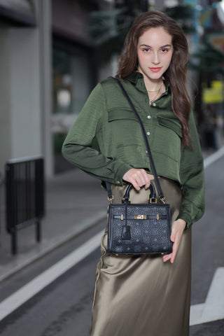 Young woman looking at the camera and carrying a stylish black Saga handbag, wearing a green blouse and beige pants on the street