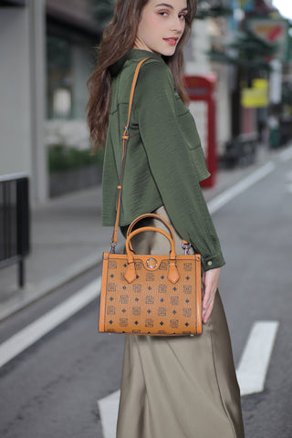 A woman dressed in an elegant outfit and carrying a beige Saga handbag with distinctive logo details, standing on the sidewalk in a modern city.