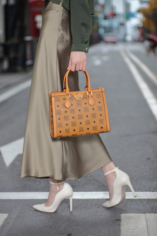 عارضة أزياء تعرض شنطة ساغا النسائية بلون بيج أثناء المشي في الشارع، مع تفاصيل الأزياء العصرية والأحذية الأنيقة.