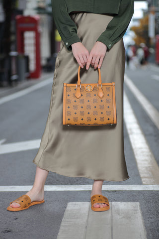 A model shows off a beige Saga women's handbag while wearing a matching color dress and open sandals that match the bag.