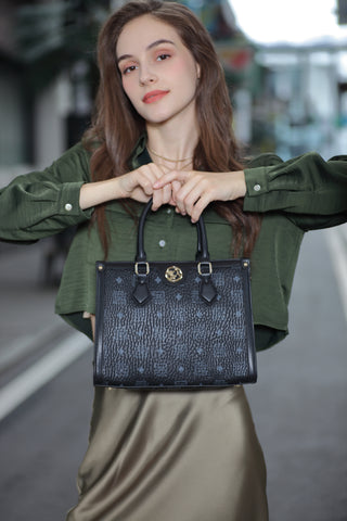 A fashion model stands in the street holding a women's black Saga bag, exuding a matching and elegant dress.