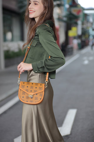 A girl walking in the street carrying a women's handbag from Saga, yellow in color, made of luxurious leather and printed with the Saga logo.