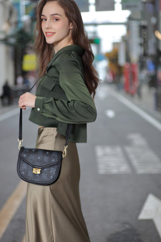 A girl carrying on her shoulder a women's handbag from Saga, black in color, engraved with the Saga logo