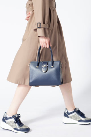 A woman walks in a beige skirt, carrying a blue leather handbag, and wearing sneakers that match the bag