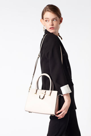 A woman stands aside, carrying a luxurious beige Saga handbag and wearing an elegant black suit