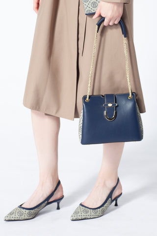 A woman carries a blue Saga women's crossbody bag with a gold chain and wears shoes with a matching pattern
