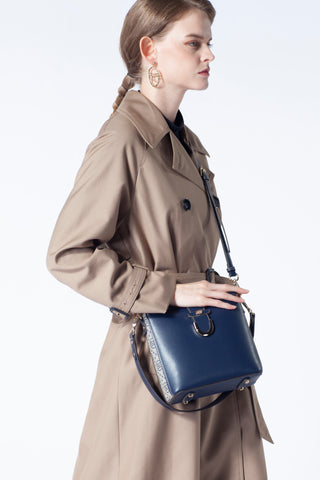 A dark blue Saga leather handbag hanging from a model's shoulder with an elegant look