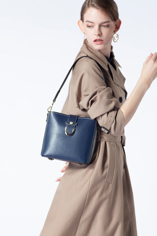 Model standing sideways carrying a navy blue Saga bag with a beige coat