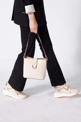 A model stands sideways carrying a beige Saga handbag featuring a modern design and delicate details.